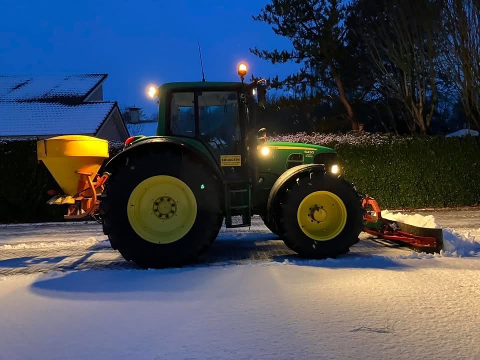 Trekker met zoutstrooier op een besneeuwde weg bij avond